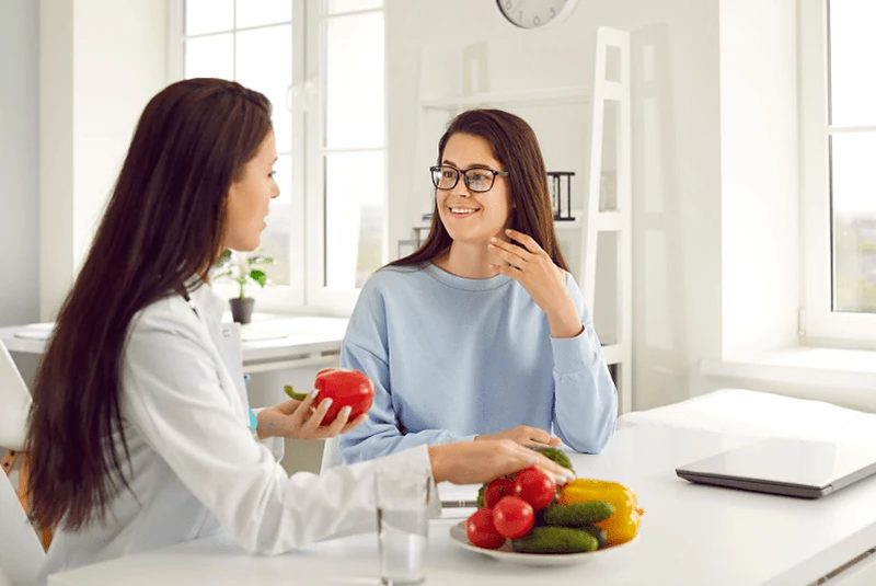 Zwei Frauen sitzen am Tisch mit frischem Gemüse und Obst im Gespräch.