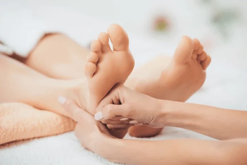 Hände halten einen Fuss für eine Fussreflexzonenbehandlung.