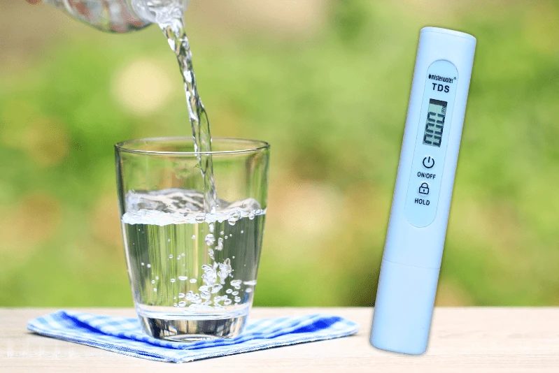 Ein Glas Wasser wird eingeschenkt, daneben ein Messstift für den TDS-Wert.